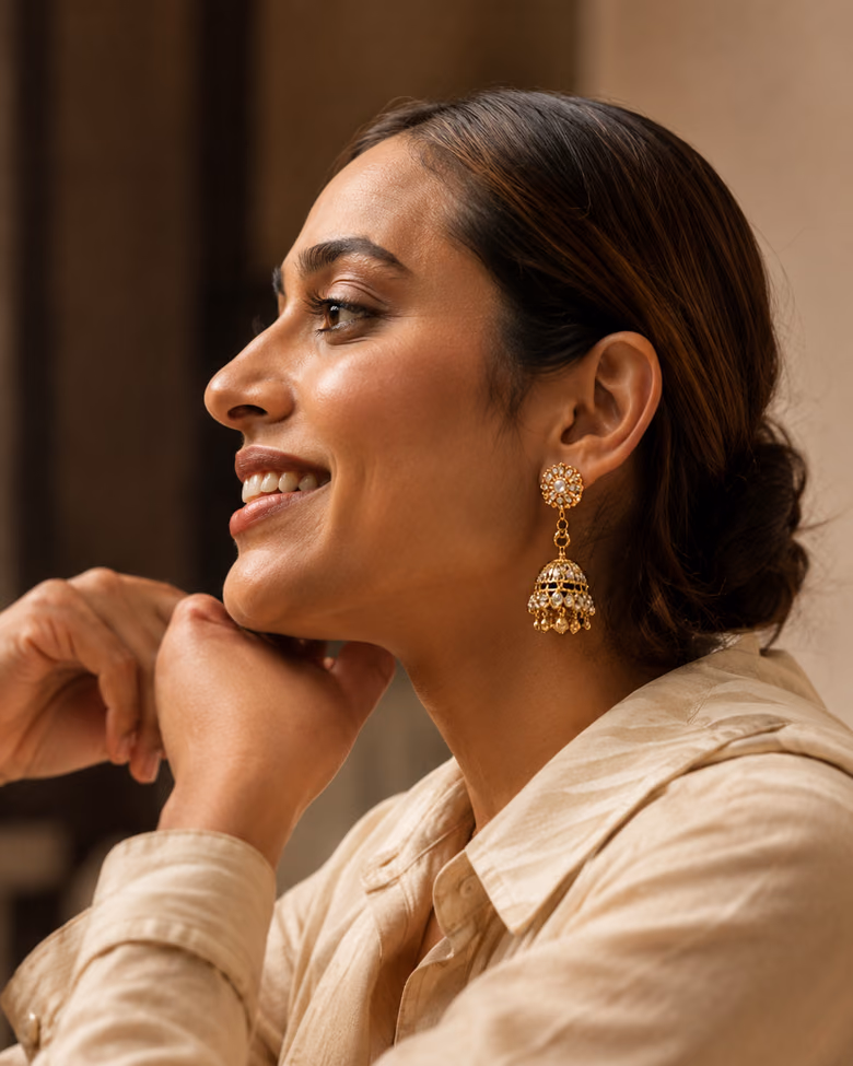 Woman smiling in profile, wearing gold jhumka earrings.